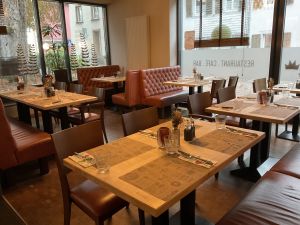 Sitzbereich im Restaurant direkt an großen Fenstern. Braune Lederstühle und -bänke an fertig gedeckten Tischen. Auf der Fensterscheibe steht spiegelverkehrt "RESTAURANT . CAFÉ . BAR".